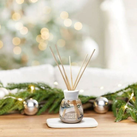 Yankee Candle amber and sandalwood reed diffuser with wooden sticks on a white tray with holiday greenery