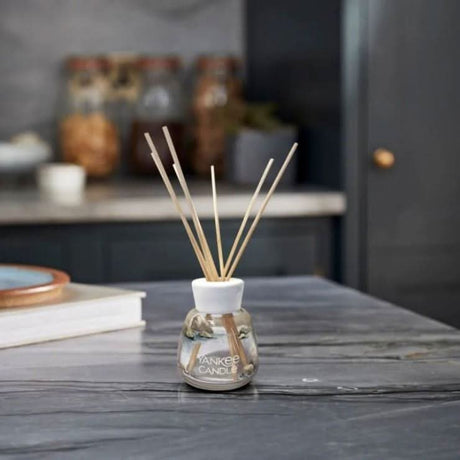 Yankee Candle amber and sandalwood reed diffuser on a kitchen countertop with books and jars in background
