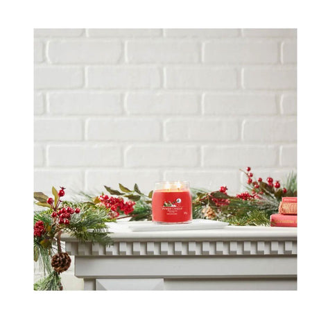 Yankee Candle Christmas Eve jar candle lit on mantel decorated with pine branches and red berries