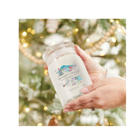 Hand holding Yankee Candle Magical Bright Lights jar candle with festive background lights