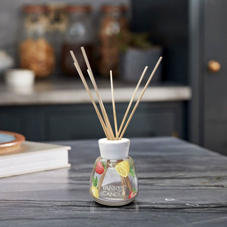 Yankee Candle reed diffuser with fruit design glass bottle and natural reeds on wooden table