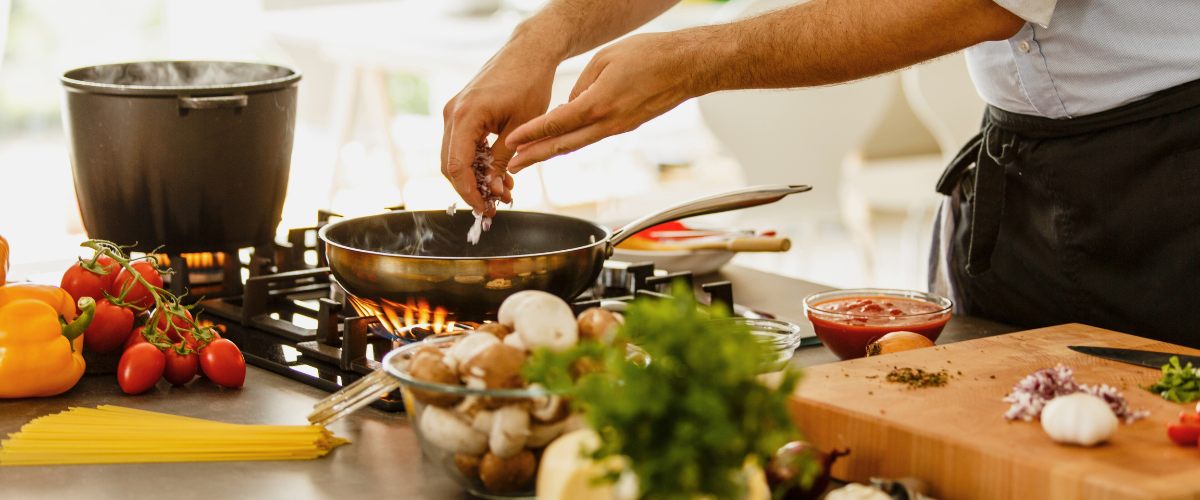 A chef cooking with must-have kitchen gadgets, vegetables, and herbs on a modern kitchen counter