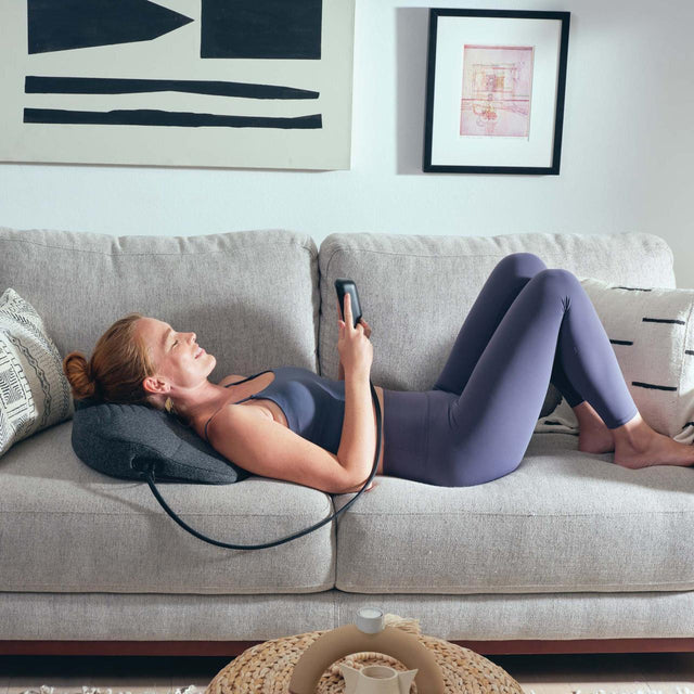 Woman relaxing on couch using electric back massagers for home with remote control in cozy living room