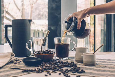 Pouring coffee from a French press with De'Longhi coffee machines brewed coffee and scattered coffee beans