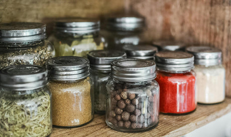 Affordable kitchen storage solutions with glass jars holding spices and dried herbs on wooden shelf