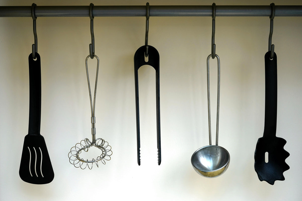 Collection of kitchen gadgets online including spatula, whisk, tongs, ladle, and pasta server hanging on a rack