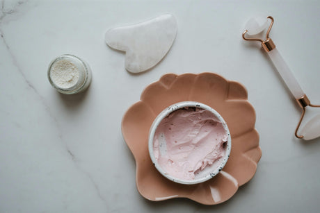 Affordable skincare products including pink face cream, jade roller, gua sha tool, and facial powder on marble surface