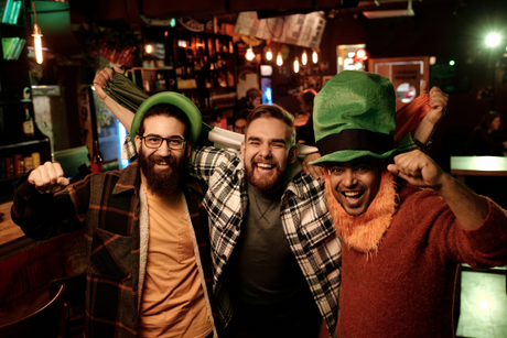 Three men celebrating in a bar wearing fun stag do costumes including a green hat and festive accessories
