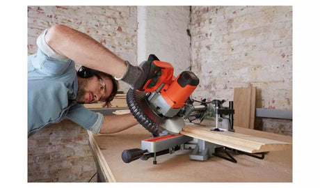 Man using an orange and black Black and Decker power tools miter saw to cut wood indoors