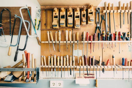 Affordable hand tools for home including saws, planes, chisels, and screwdrivers organized on a wooden wall