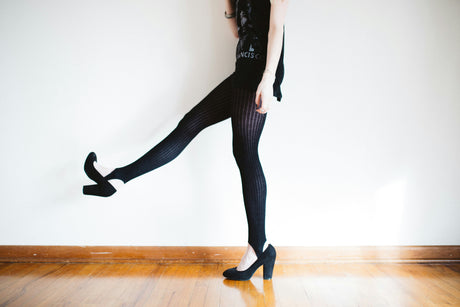 Woman wearing black stylish women's tights for sale paired with high heels against a white wall