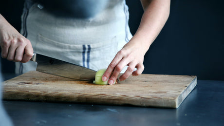 Person using knife on wooden cutting board showcasing essential food preparation tools