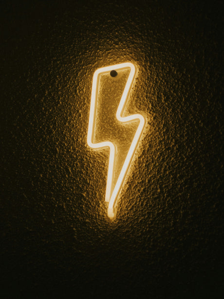 Glowing yellow lightning bolt neon sign on dark textured wall representing Black Friday electrical deals