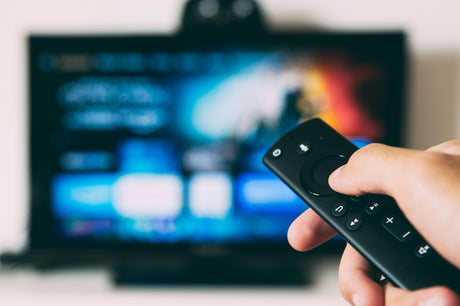 Hand holding remote control in front of a TV screen showcasing film and video game merchandise options