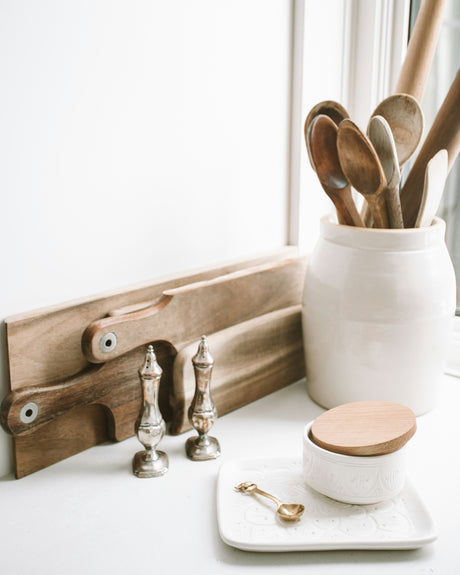 Affordable homeware deals with wooden utensils, ceramic jar, salt and pepper shakers on a white kitchen countertop