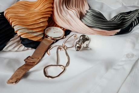 Women's fashion accessories including a watch, earrings, and a colorful pleated scarf on a white shirt