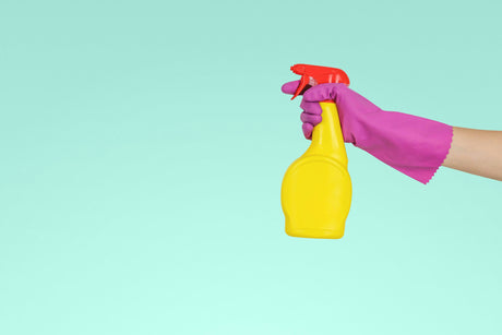 Hand wearing pink glove holding yellow spray bottle cleaning products online for home cleaning tasks