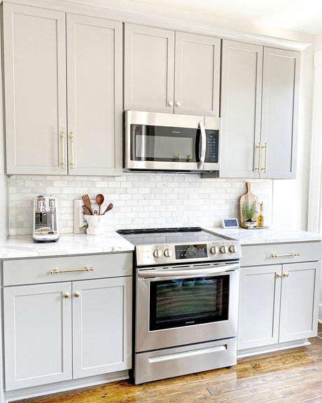 Modern kitchen with stainless steel oven and microwave surrounded by small kitchen appliances on white marble countertops
