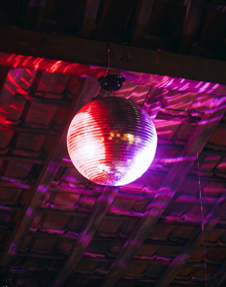 Shiny disco ball hanging from wooden ceiling with colorful purple and red party decorations online lighting