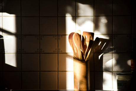 Wooden kitchen utensils set in a holder on kitchen counter with tiled backsplash and natural light