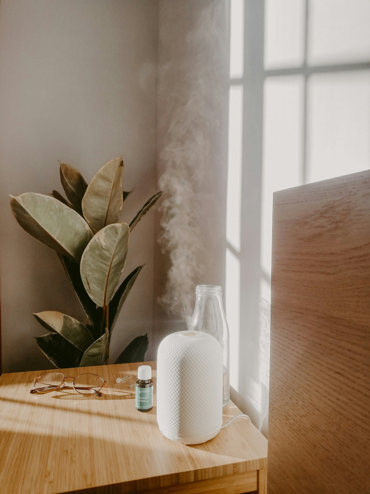 Best home diffusers releasing calming mist on wooden table next to plant and eyeglasses in sunlight