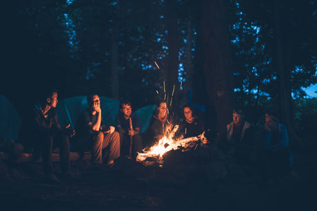 Group of people camping at night around a campfire with tents in the background camping gear online