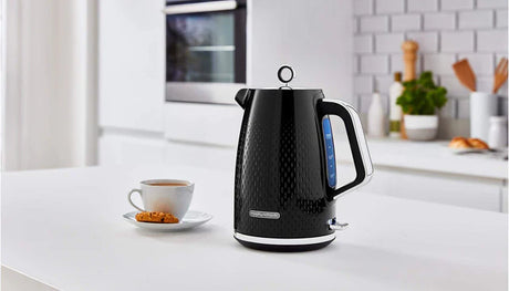 Black textured electric kettle from Morphy Richards appliances on a white kitchen counter with a cup of coffee and cookie