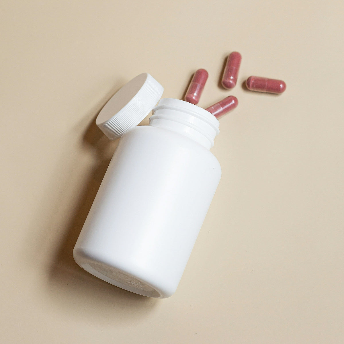 White supplement bottle with pink capsules spilling out representing health supplements online