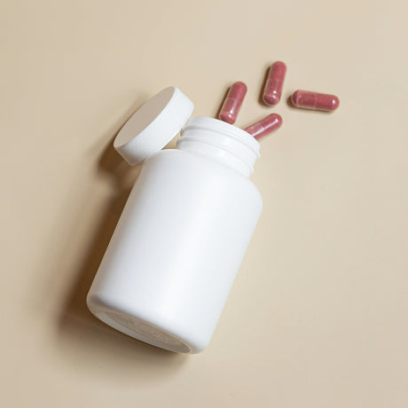 White supplement bottle with pink capsules spilling out representing health supplements online