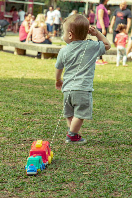 Toddler playing with colorful pull-along toy in park using outdoor toys for kids on grassy field