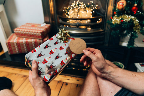 Hands holding a wrapped present with a Santa tag in a cozy living room for secret santa gifts under £5