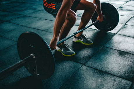 Person lifting a barbell on a gym floor showcasing home workout equipment for strength training