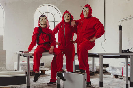 Three people wearing adult money heist jumpsuit with red hood and mask in an industrial setting