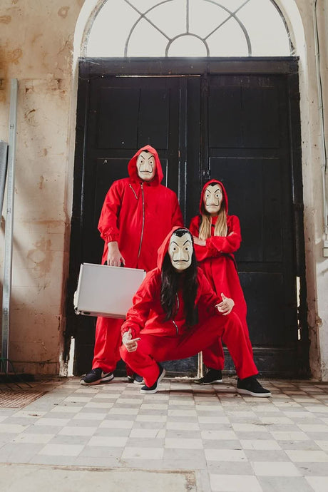 Three people wearing adult money heist jumpsuit with red hooded suits and Salvador Dalí masks posing indoors