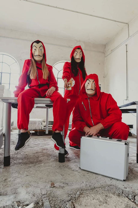 Three people wearing adult money heist jumpsuit red hooded costumes with Salvador Dalí masks indoors