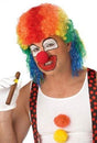 Adult man wearing an adult rainbow clown wig with red nose and colorful face paint holding a cigar