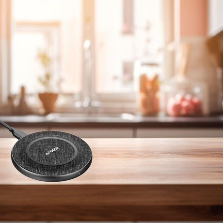 Anker wireless charging pad with fabric texture on wooden table in bright kitchen setting