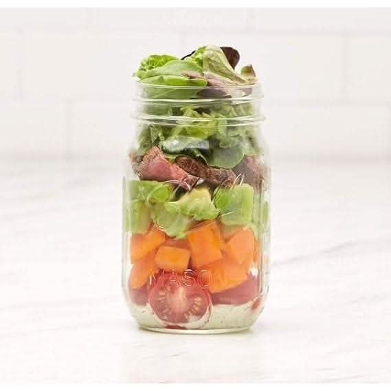 Ball wide mouth mason jars filled with fresh layered salad ingredients including lettuce tomatoes and avocado
