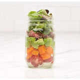 Ball wide mouth mason jars filled with fresh layered salad ingredients including lettuce tomatoes and avocado