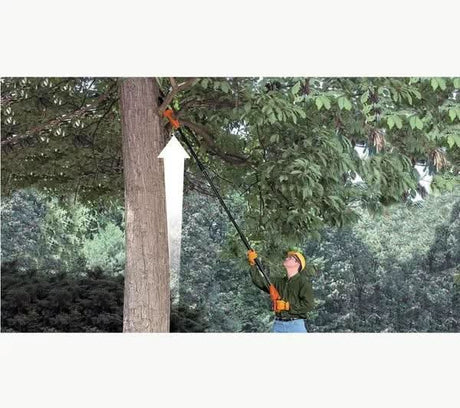 Person using cordless pole pruner to trim high tree branches with safety gear in outdoor setting