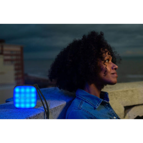 CLICKK Home Store portable speaker black emitting blue light beside a woman sitting outdoors at dusk