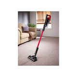 Red and black cordless stick vacuum cleaner standing on carpet in modern living room