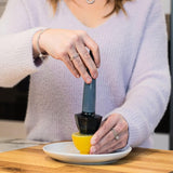 Calitek ergonomic lemon reamer in black used to extract juice from a lemon half on white plate