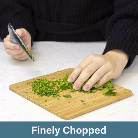 Calitek herb chopper mezzaluna finely chopping fresh green herbs on a wooden cutting board