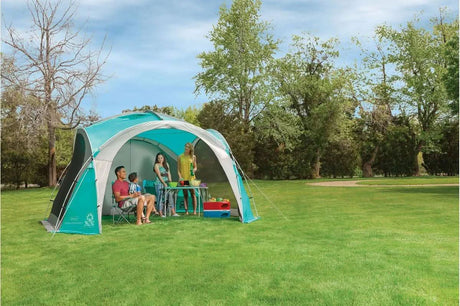 Coleman Event Dome tent set up in a grassy park with people sitting and standing inside the blue and gray gazebo