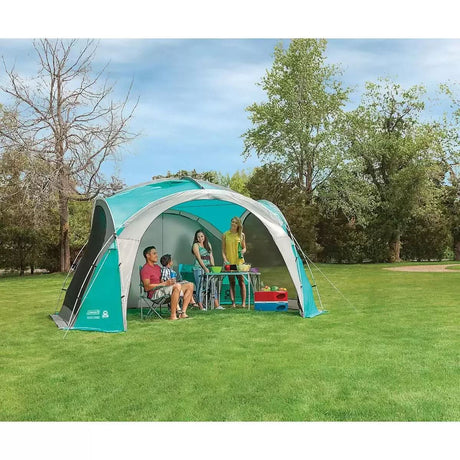 Coleman Event Dome XL shelter set up on green grass with family sitting and standing inside enjoying outdoor activities