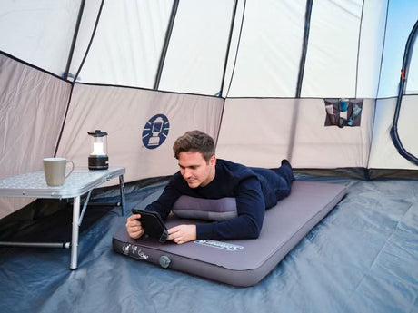 Man lying on gray self inflating sleeping mat inside a camping tent using a tablet