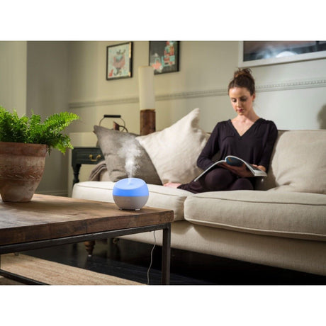 Homedics color changing essential oil diffuser on a coffee table with a woman relaxing on a sofa