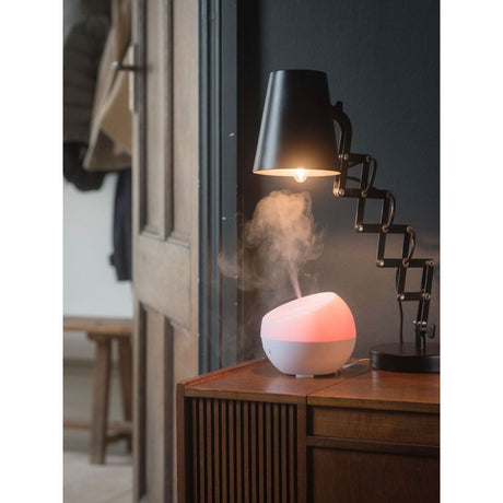 Homedics color changing essential oil diffuser emitting steam beside a modern lamp on a wooden table