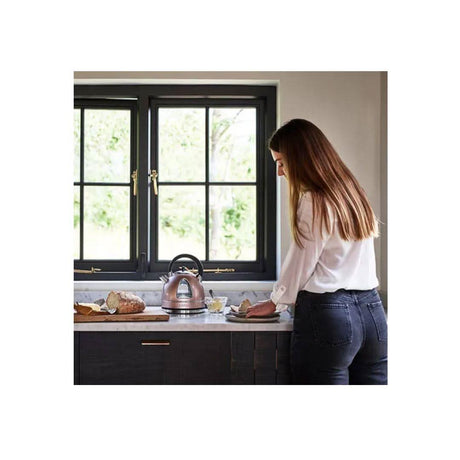 Woman using a Cuisinart stainless steel kettle on a kitchen countertop near window